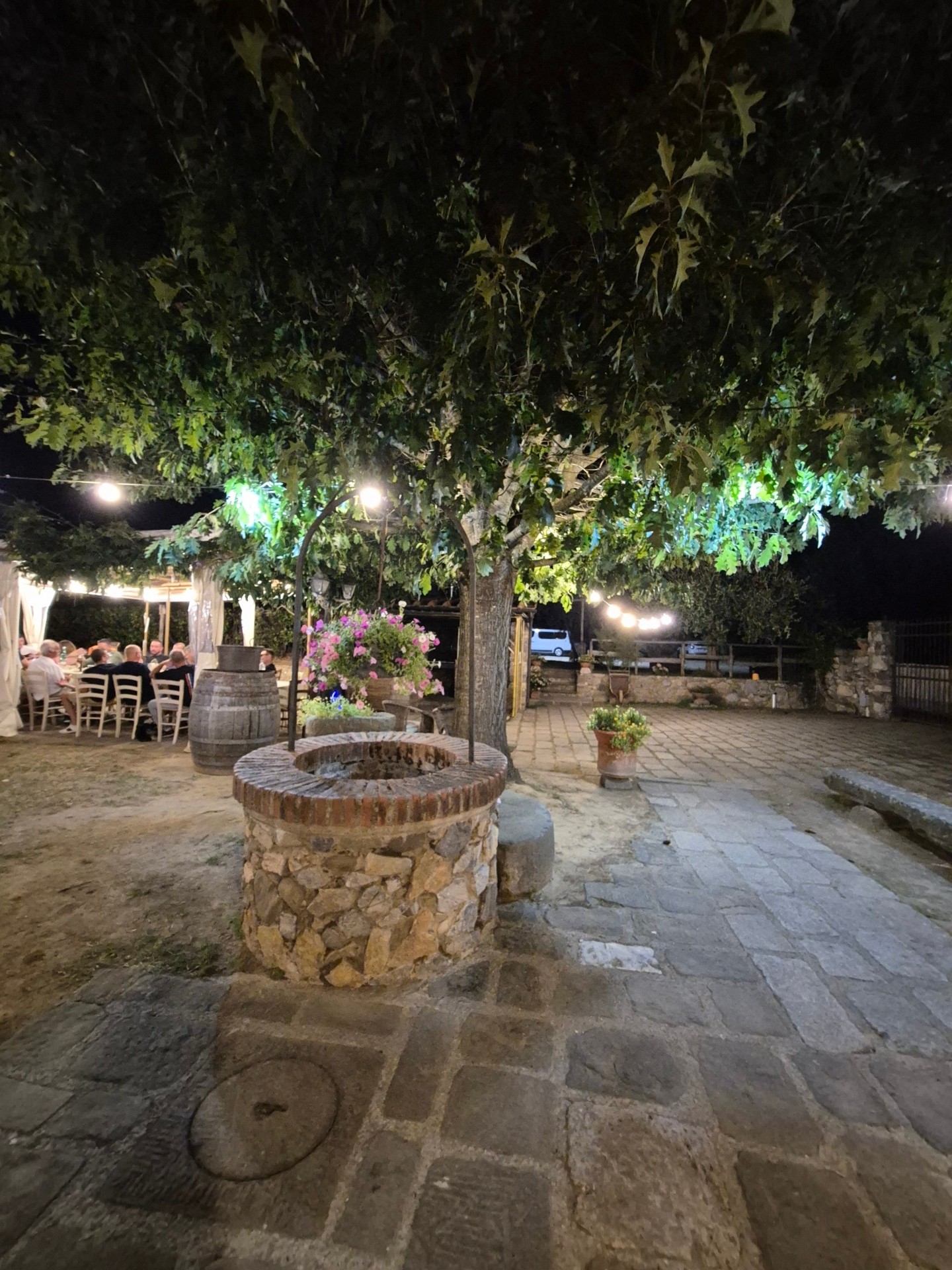 Pozzo in pietra con ospiti a tavola sotto la quercia