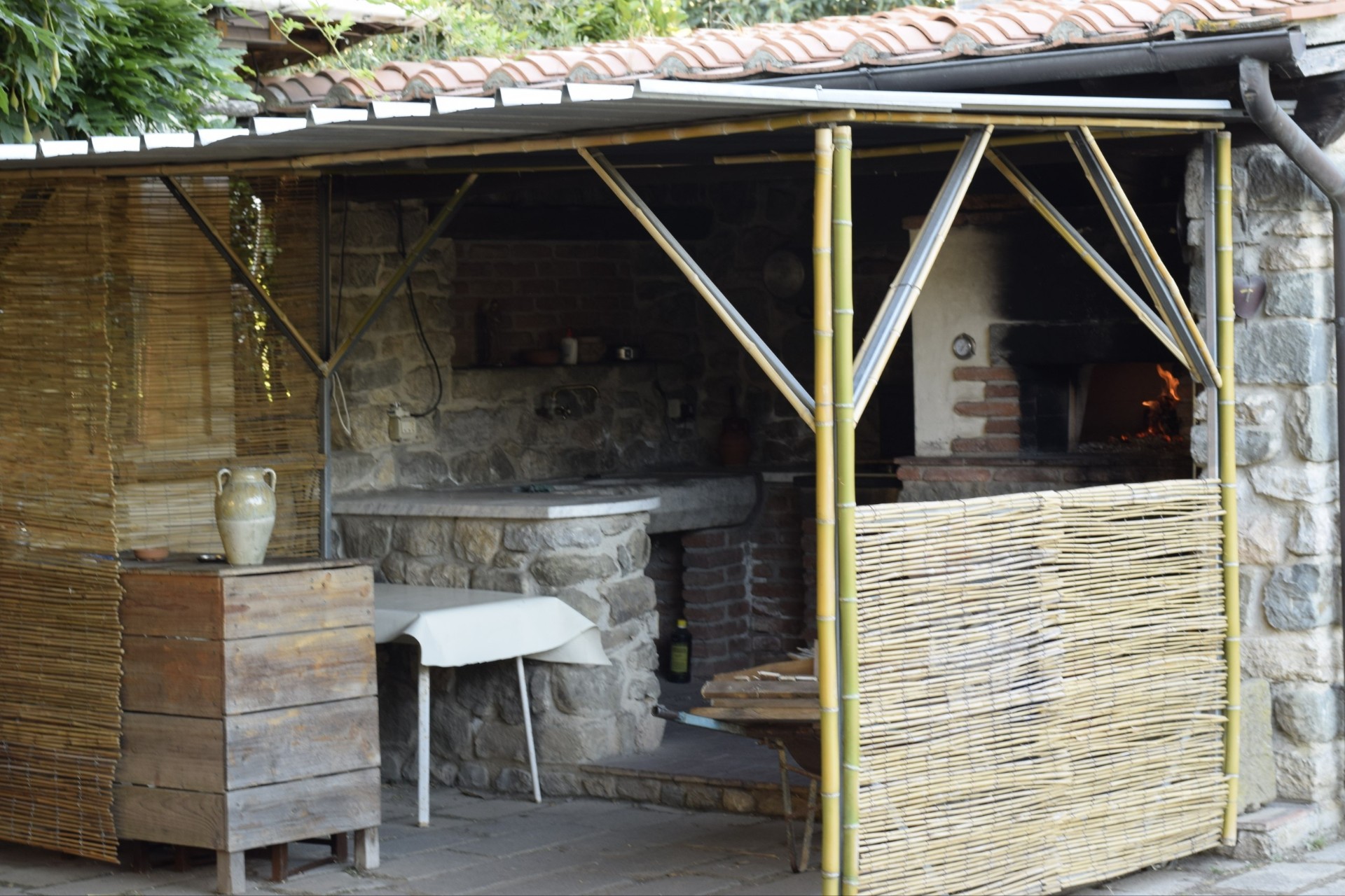 Cucina esterna con forno a legna e pergola in bambù